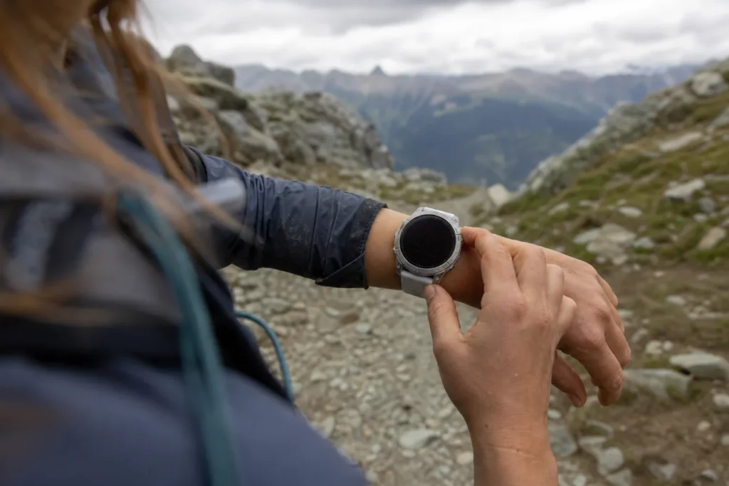 Traileuse réglant une montre GPS claire sur un sentier rocheux de montagne. Garmin vs Suunto en trail?