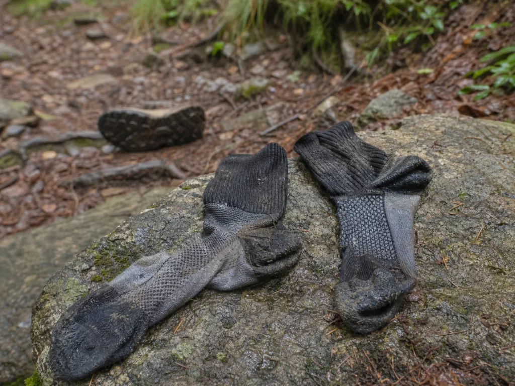 Deux chaussettes techniques humides et boueuses posées sur un rocher au bord d’un sentier