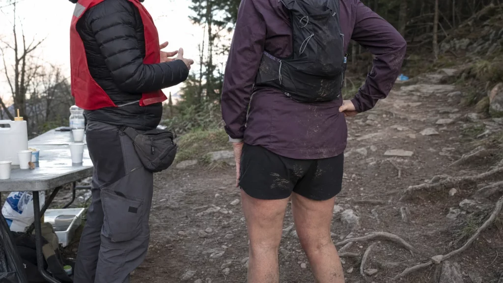 Une coureuse de dos échange avec un membre de l'assistance sur un poste de trail