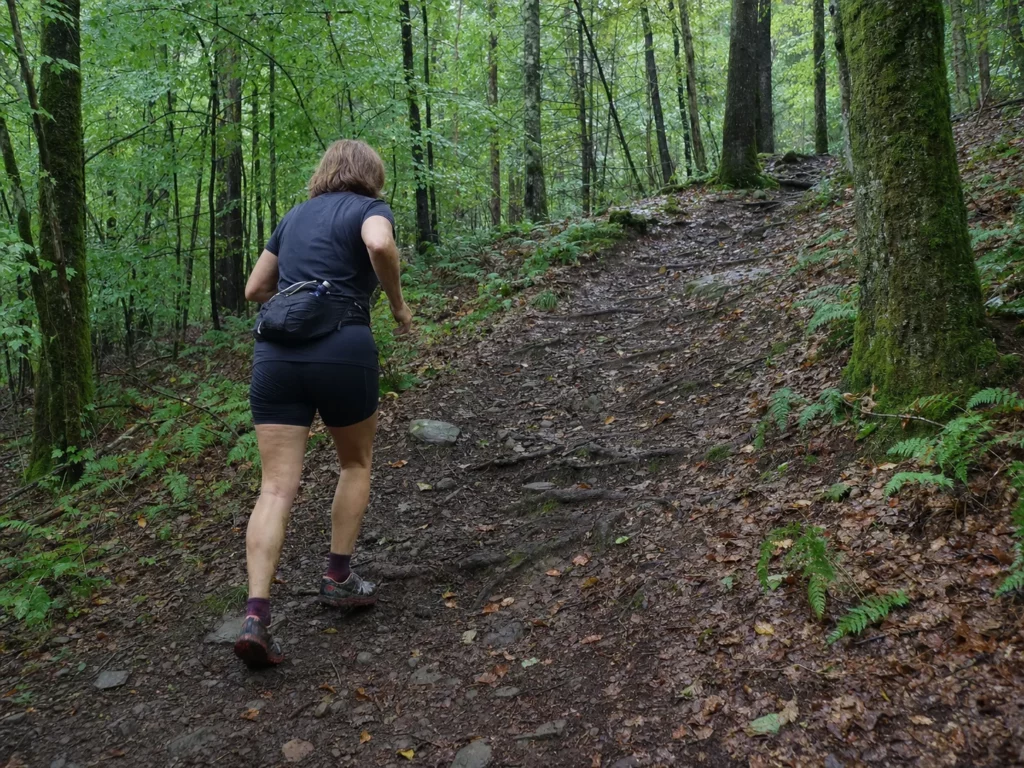 Faut-il courir ou marcher en montée ? Cette femme court sur un sentier forestier humide en pente modérée.