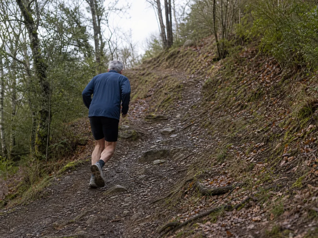 Coureur âgé vu de dos pendant une répétition sur un sentier en côte