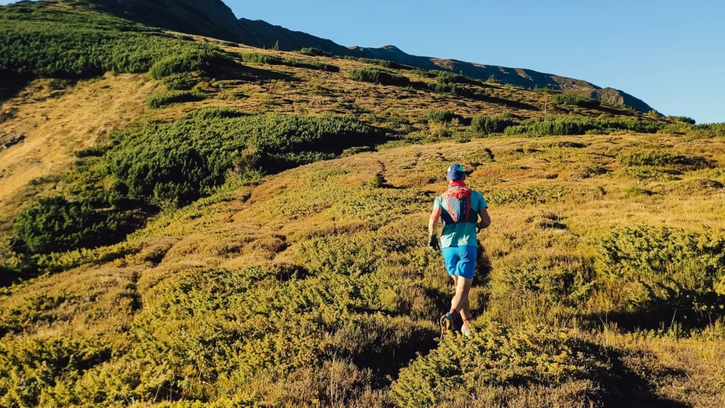 Coureur de dos progressant sur un sentier montagneux exposé au soleil