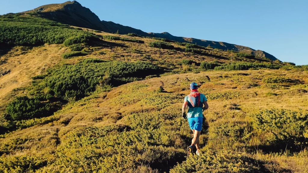 Un traileur vu de dos progresse avec son sac d'hydratation sur un sentier de montagne