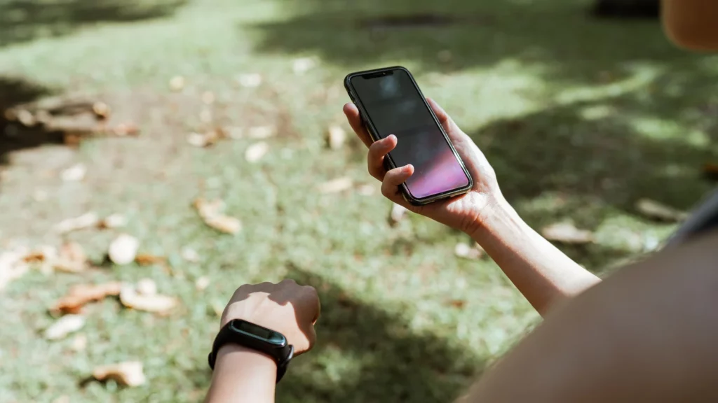 Personne comparant un bracelet de suivi sportif et un téléphone après un effort