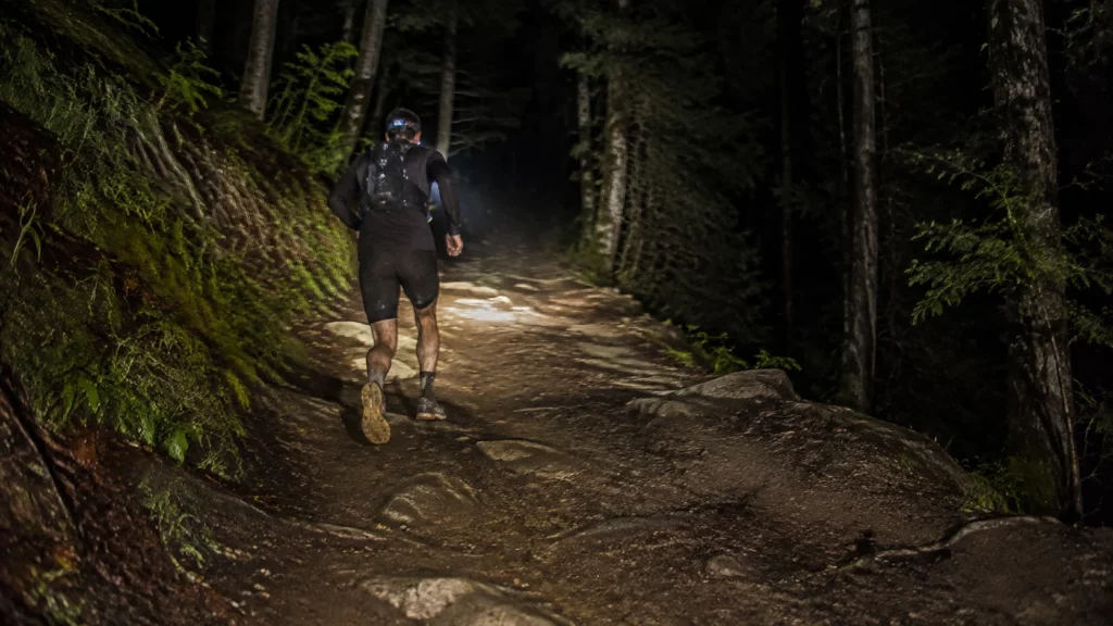 Coureur de dos progressant à la frontale sur un sentier rocheux en forêt la nuit