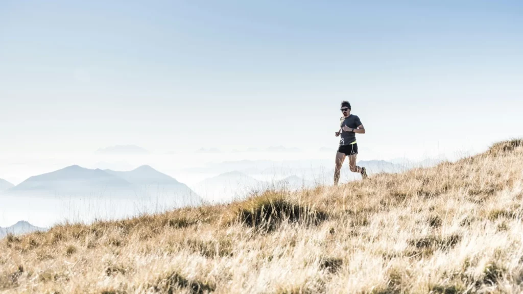 Coureur de montagne progressant sur une pente avec plusieurs sommets à l'horizon