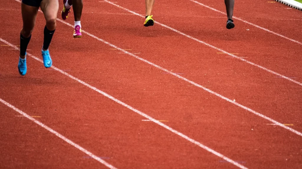 Jambes de plusieurs coureurs lancés dans leurs couloirs sur une piste rouge